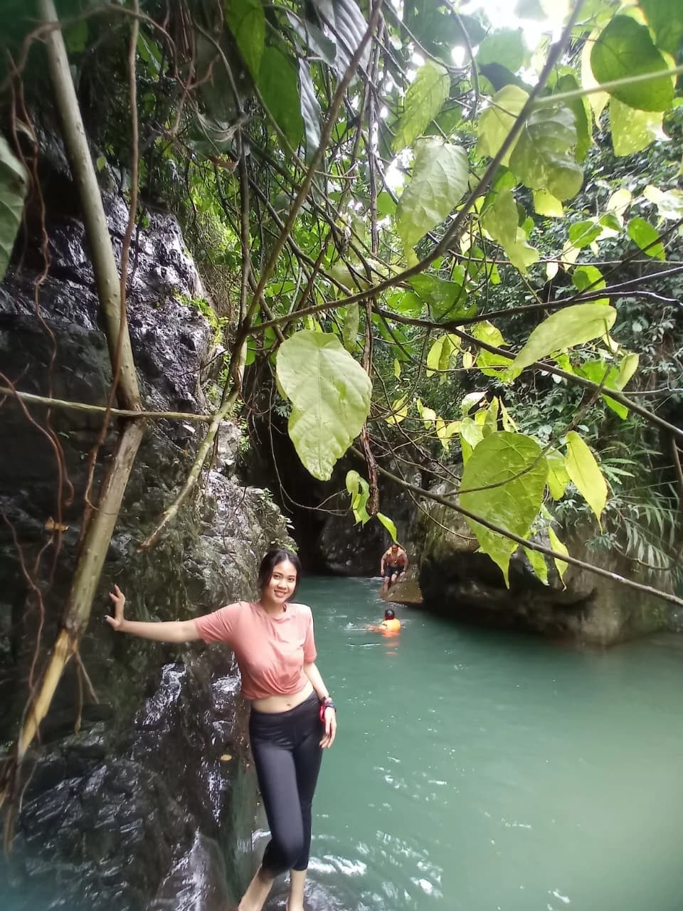 Peserta wanita tersenyum saat menyeberangi sungai dengan bantuan tongkat trekking.