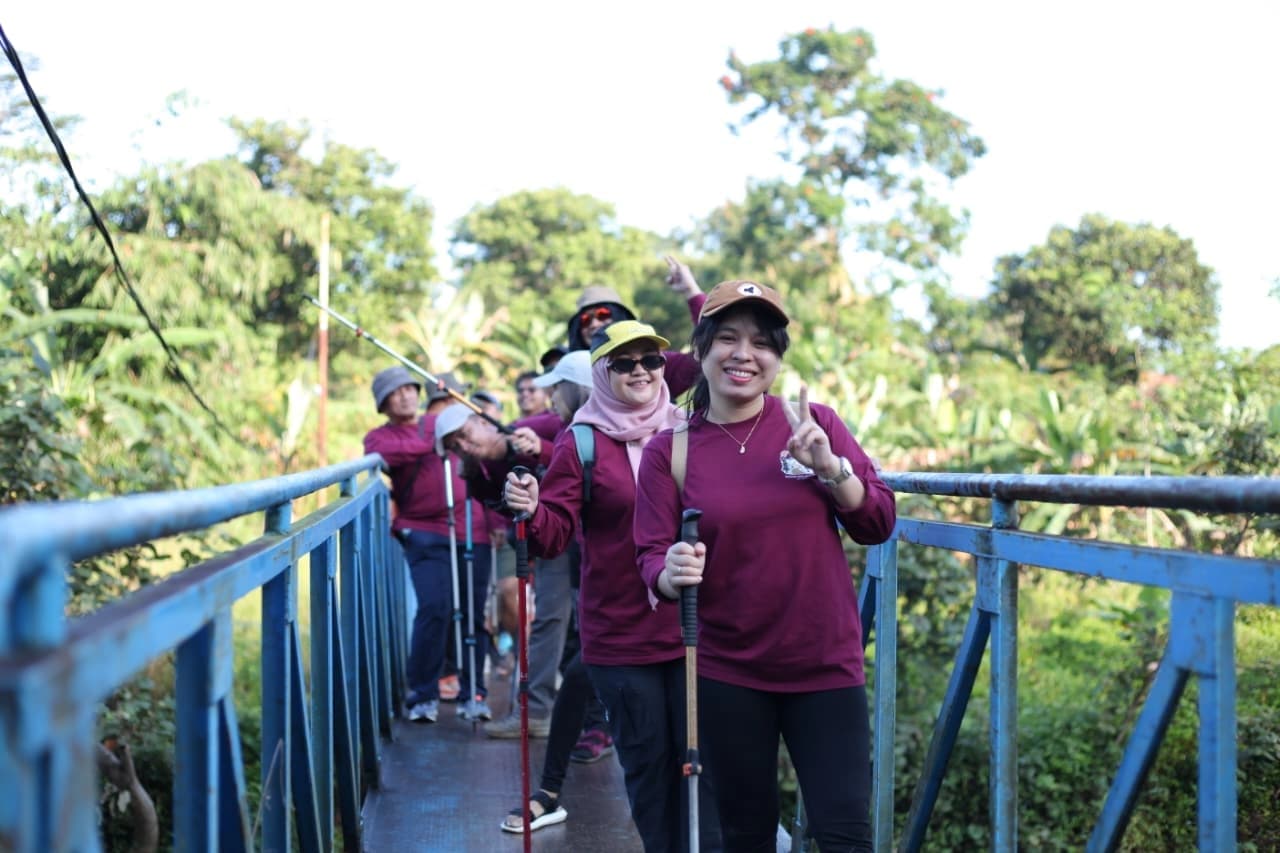 Sekelompok peserta mengangkat tongkat trekking mereka dengan semangat di depan air terjun.