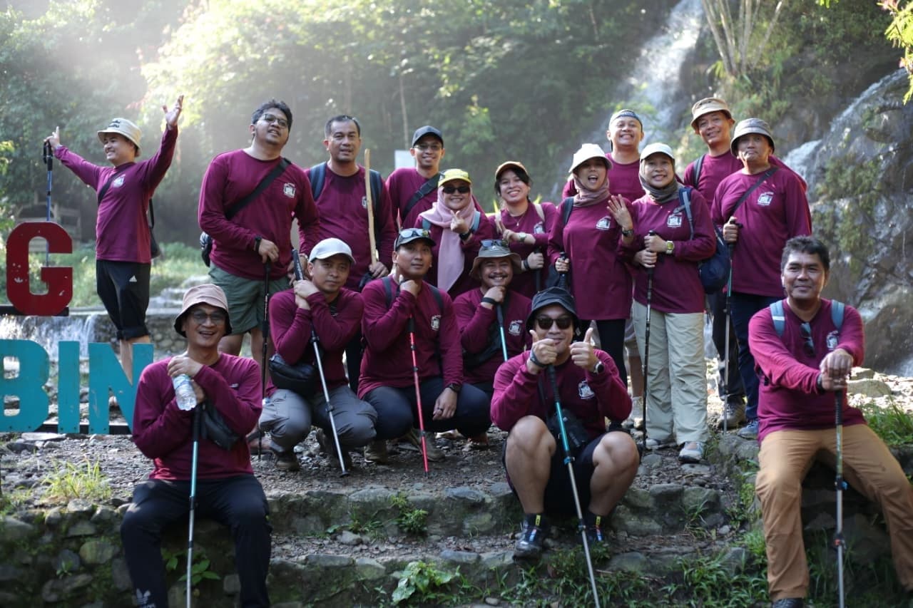 Sekelompok peserta berpose ceria dengan latar belakang air terjun yang tinggi.